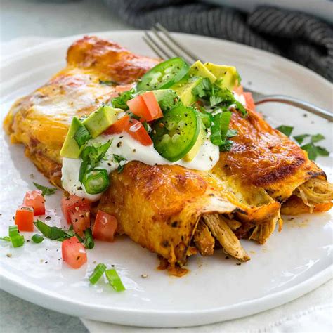 Enchiladas de pollo cubiertas con salsa mexicana y queso, acompañadas de guacamole y ensalada