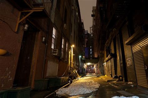 an alleyway in the city at night with snow on the ground and buildings ...