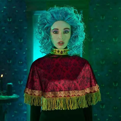 a woman with blue hair wearing a red dress and fringed shawl in a dark room