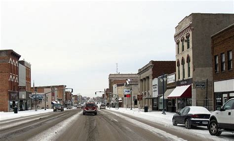 cars driving down a snowy street in the middle of town