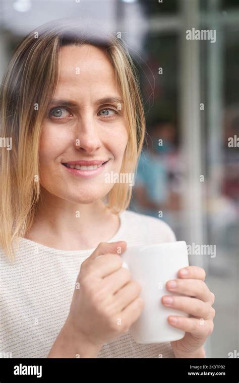 Mid-shot portrait of woman holding a coffee mug while looking through a window Stock Photo - Alamy