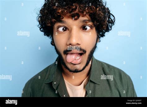 Close up face of indian or arabian curly funny guy, making a funny face, tongue out, squinted ...