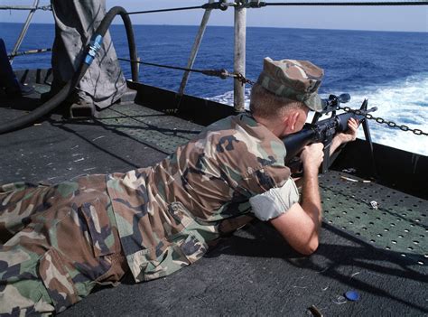 A Marine fires a scope-equipped M16A1 rifle from the fantail of the ...