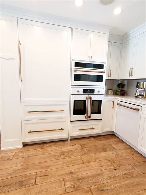 a kitchen with white cabinets and wood flooring is pictured in this image, there are two ovens ...