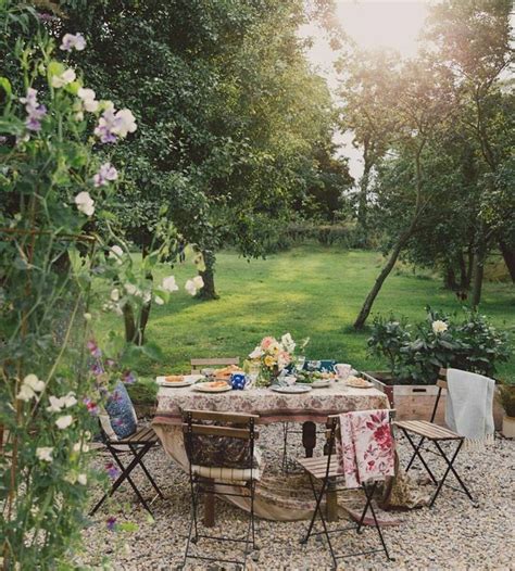 an outdoor table and chairs set up in the middle of a graveled area with flowers