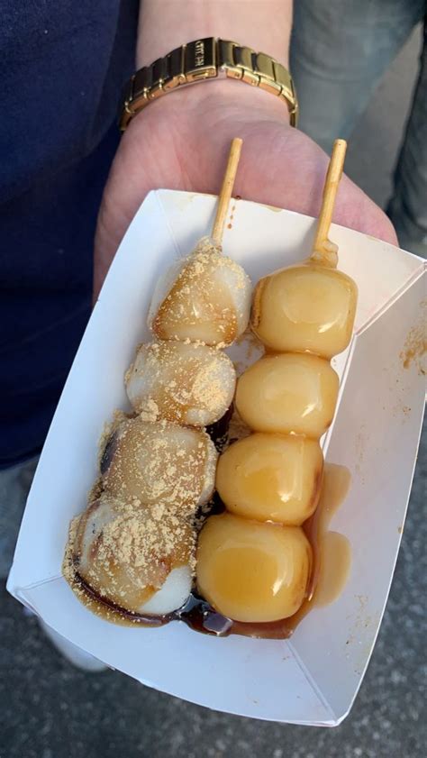 a person holding a paper container with food in it and some skewers ...