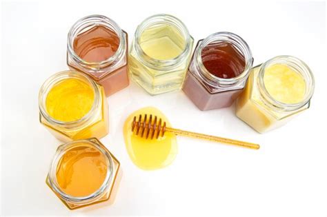 Premium Photo | Spoon with fresh honey and jars with different types of honey on a white ...