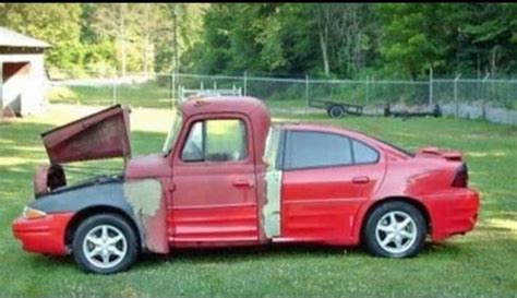 a red car with its hood open sitting on the grass in front of a fence