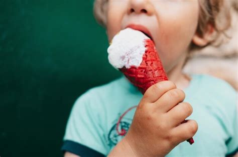 Premium Photo | A young boy eating a red ice cream cone with a white fluffy cone in his hand.