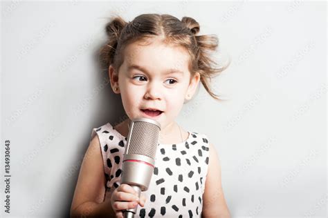 Happy Cute little girl singing a song on microphone. Grey background ...