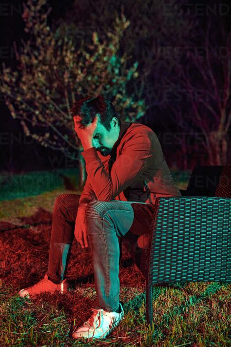 Sad man sitting alone on garden bench at night stock photo