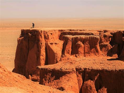 a man standing on top of a cliff in the middle of some desert land,