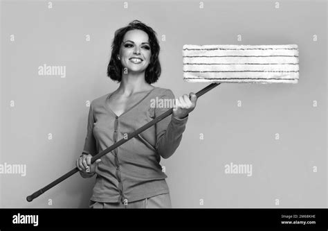 Happy young woman holding mop for doing chores beige background ...