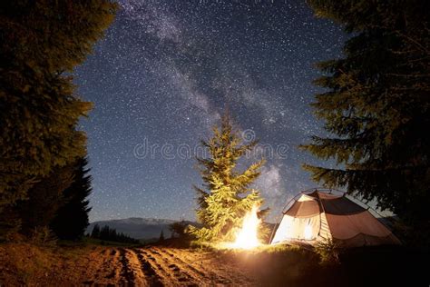 Night Camping in Mountains. Tourist Tent by Campfire Near Forest Under Blue Starry Sky, Milky ...