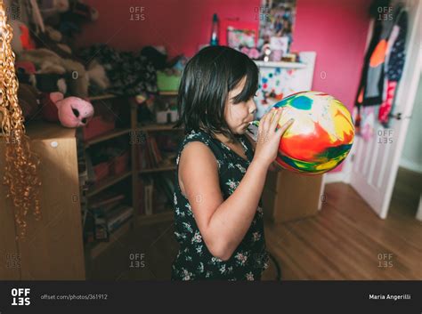 Young girl blowing up a colorful balloon stock photo - OFFSET