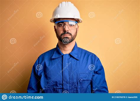 Mechanic Man with Beard Wearing Blue Uniform and Safety Glasses Over Yellow Background with ...