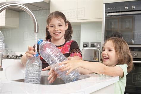 Girls filling up water bottle in kitchen - Stock Photo - Dissolve