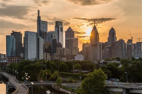 the sun is setting over a city with skyscrapers and trees in the foreground