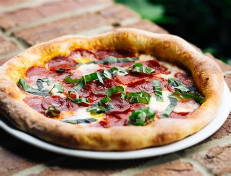 a pepperoni and basil pizza on a white plate sitting on a brick patio table