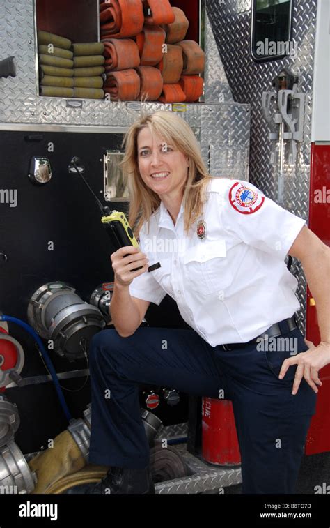 Smiling Female firefighter paramedic EMT in dress uniform talking on two way radio in front of ...