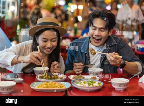 Young Asian couple traveler tourists eating Thai street food together in China town night market ...