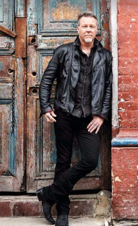 a man standing in front of a wooden door wearing a leather jacket and black pants