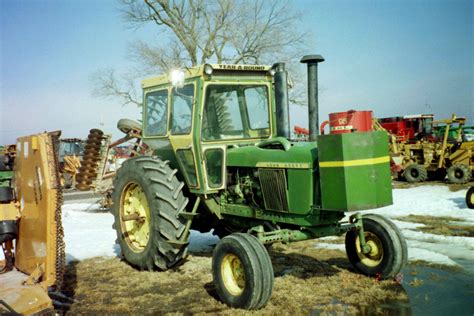 a green tractor parked next to other tractors in a field with snow on ...