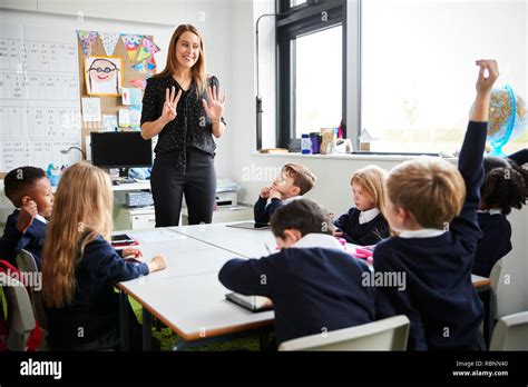 Female primary school teacher standing in a classroom gesturing to ...