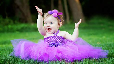 Cute Smiley Girl Baby Is Sitting On Green Grass Wearing Purple Frock And Flower Band On Head ...