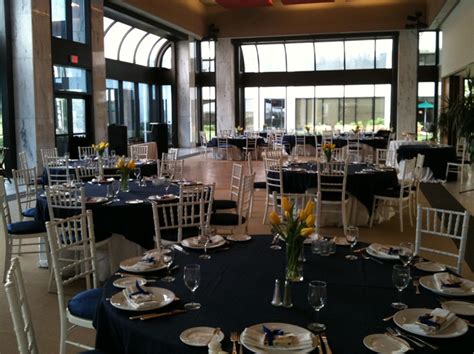 tables set up for an event with black linens and white chairs, blue tablecloths and yellow flowers