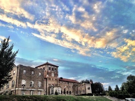 an old brick building sitting on top of a lush green field under a cloudy blue sky