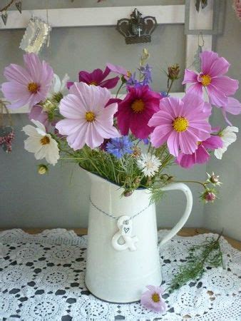 a white pitcher filled with lots of purple flowers on top of a doily covered table