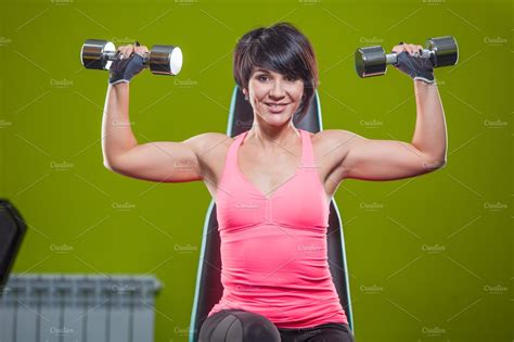 Gym woman strength training lifting dumbbell weights in shoulder press exercise. Female fitness ...