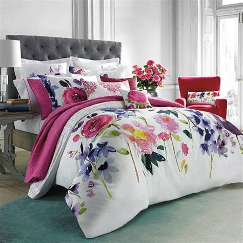 a bed with pink and purple flowers on it in a room next to a red chair