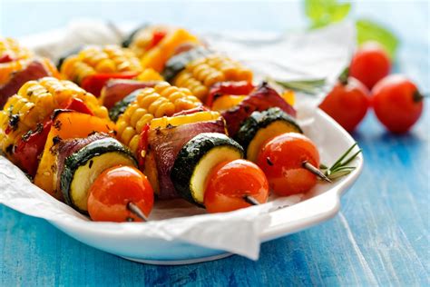 an assortment of vegetables on skewers in a white dish next to tomatoes ...