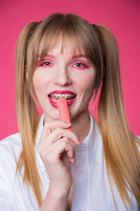 Portrait of a Young Woman with Braces and Bright Makeup Chewing Gum on a Pink Background ...