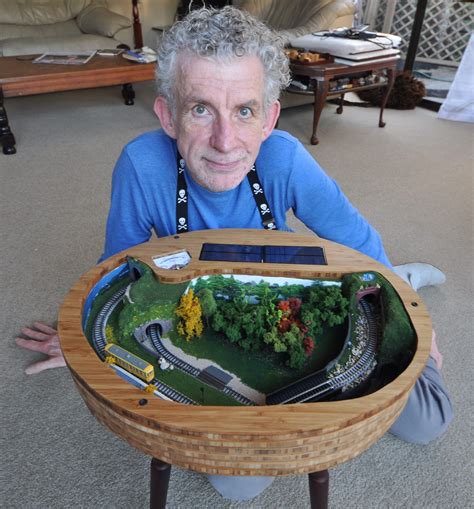 an older man is holding up a model train set on a table with a mirror