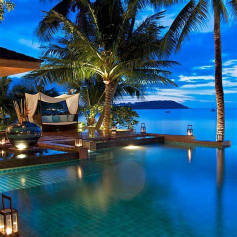 an outdoor swimming pool surrounded by palm trees and lights at night ...