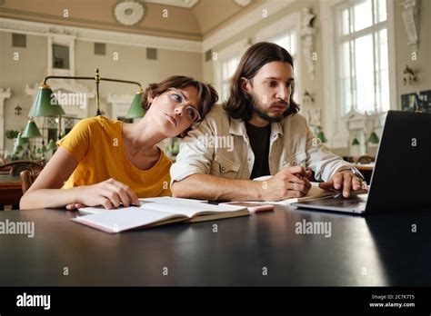 Two young students tiredly working on study project with laptop in ...