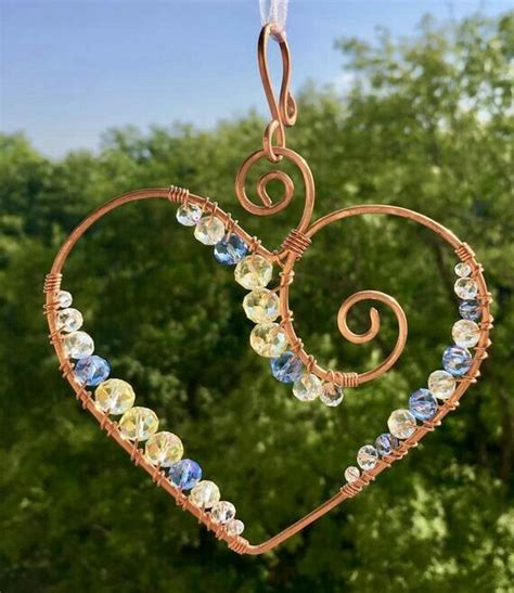 a heart shaped ornament hanging from a wire with crystal beads and copper spirals