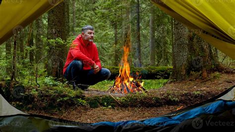 Bearded man by the fire in a beautiful forest. The camping is located in a beautiful forest lawn ...