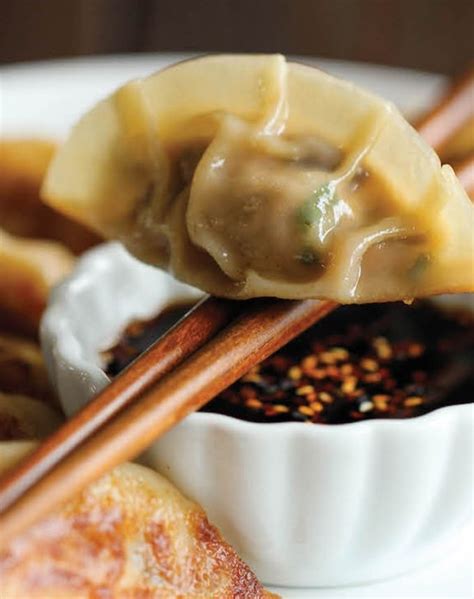 chopsticks are holding dumplings with sauce in the bowl and on top of them