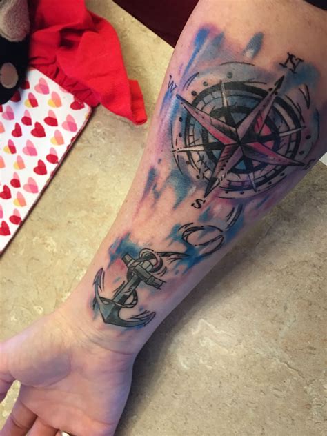 a person with a tattoo on their arm holding an anchor and compass in the background