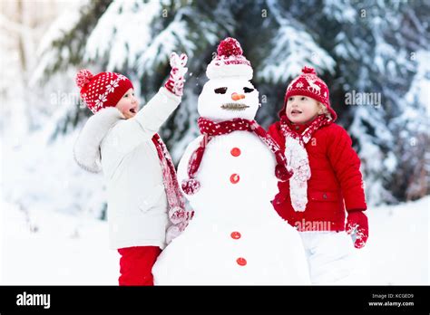 Children build snowman. Kids building snow man playing outdoors on sunny snowy winter day ...