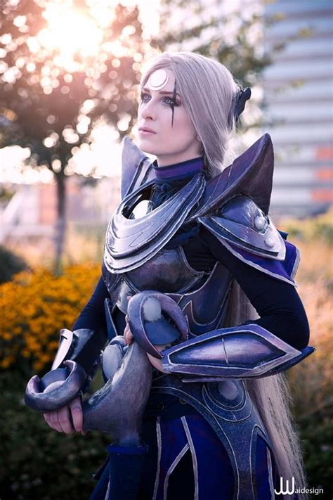 a woman dressed in armor and holding a helmet on her shoulder with the sun shining behind her