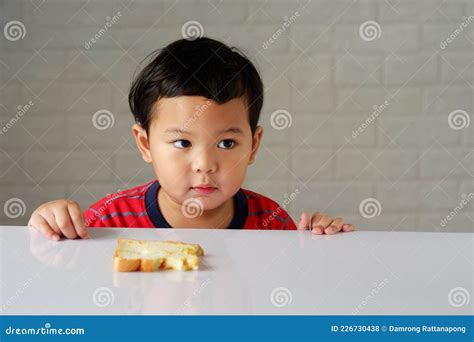 Cute Little Asian Boy Has an Bored Expression and is Eating Bread on a White Dining Table Stock ...
