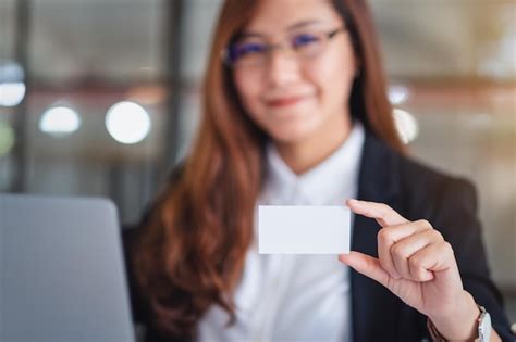 Premium Photo | Portrait of businesswoman holding blank card while using laptop at desk in office