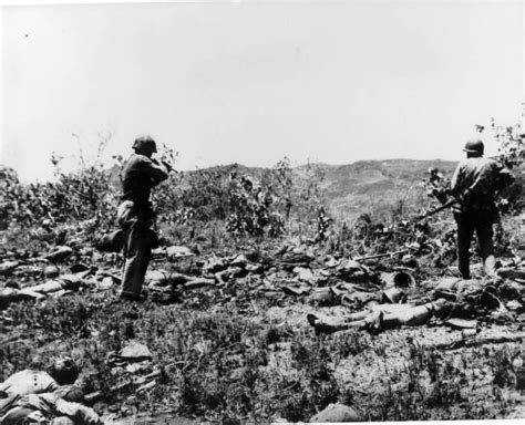 Two Marines pick their way through dead Japanese troops following a ...