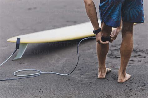 Surfer at the beach attaching surfboard leash stock photo