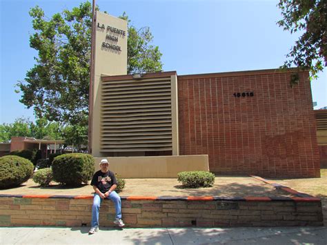 a man sitting on the side of a brick wall in front of a large building